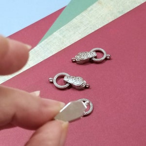 May include: Three silver-toned metal clasps with ornate designs. The clasps are on a red surface.