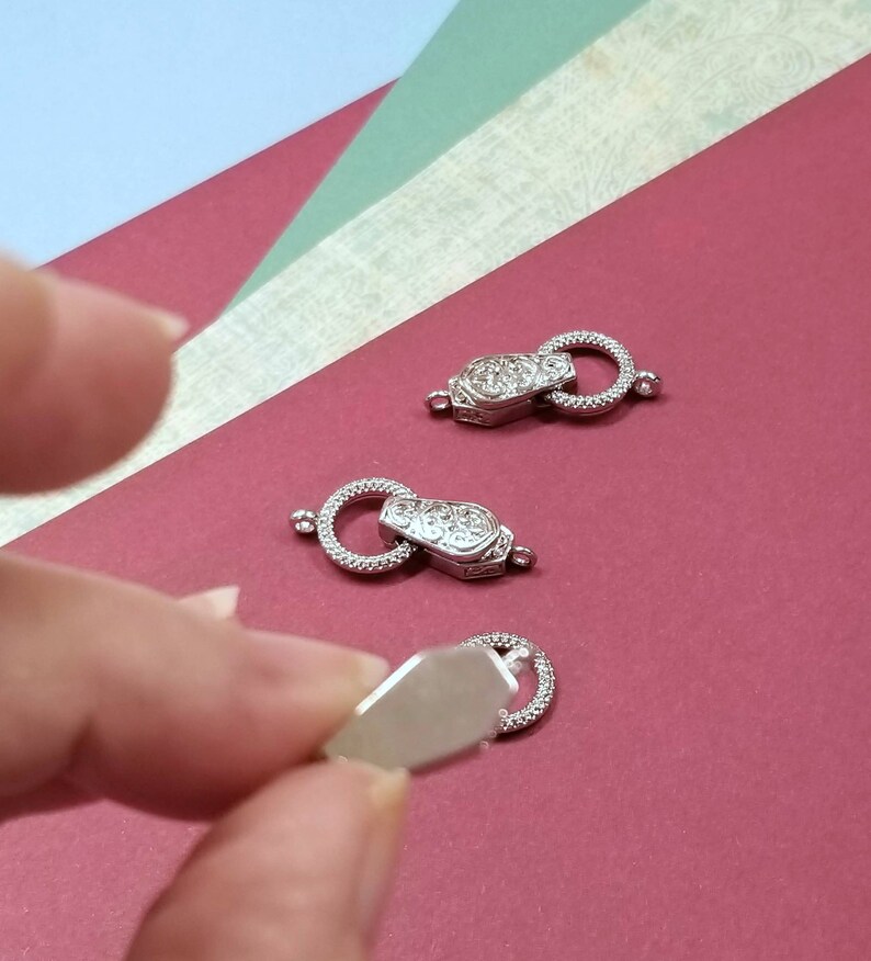 May include: Three silver-toned metal clasps with ornate designs. The clasps are on a red surface.