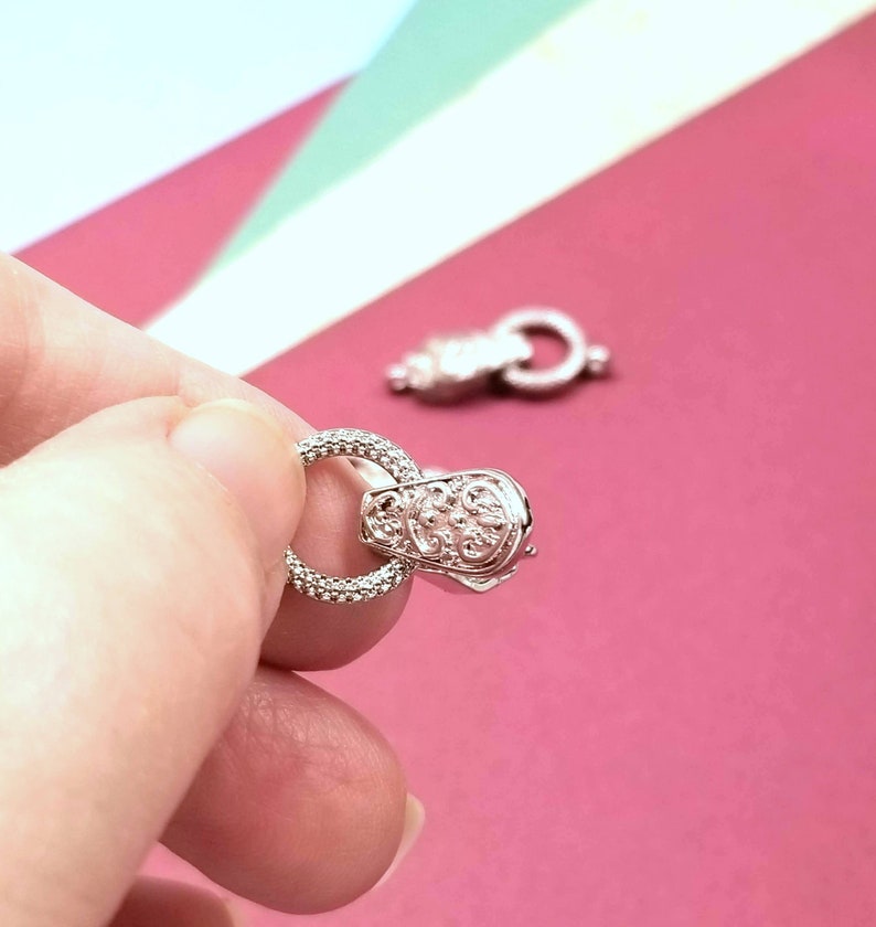 May include: Silver-toned metal clasp with a decorative design and a round ring. The clasp is designed for jewelry making.