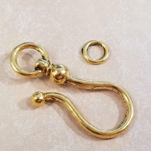 May include: A gold-toned metal swivel clasp with a round loop and a decorative ball. The clasp is designed to attach to a chain or other jewelry.