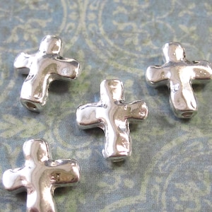 May include: Four silver metal cross-shaped beads. The beads have a textured, hammered finish.