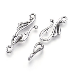 May include: Three antique silver-colored jewelry clasps. The clasps have an ornate, swirling design with a hook and eye closure. The largest clasp is approximately 2 inches long. The smallest clasp is a simple loop.