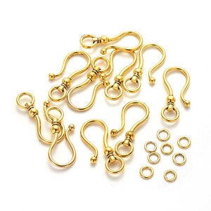 May include: A set of 10 gold-toned metal lobster claw clasps with a decorative ball accent. The clasps are arranged in a circle on a white background. There are also 10 gold-toned jump rings included.