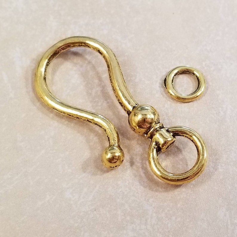 May include: Gold-toned metal swivel hook with a round loop and two ball accents. The hook is attached to a smaller, round jump ring.