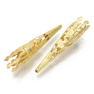 May include: Two gold metal cone-shaped bead caps with intricate filigree designs. The caps have a pointed tip and a wide, open top.