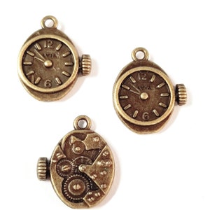 May include: Three antique gold-toned metal watch charms. Two charms feature a clock face with Roman numeral markings and a small hand. The third charm features a detailed clockwork design.