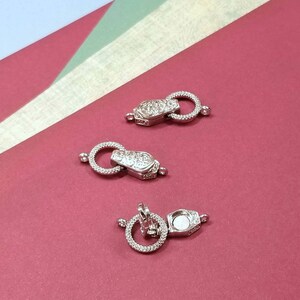 May include: Three silver-toned metal clasps with a round ring and a decorative design. The clasps are on a red surface.