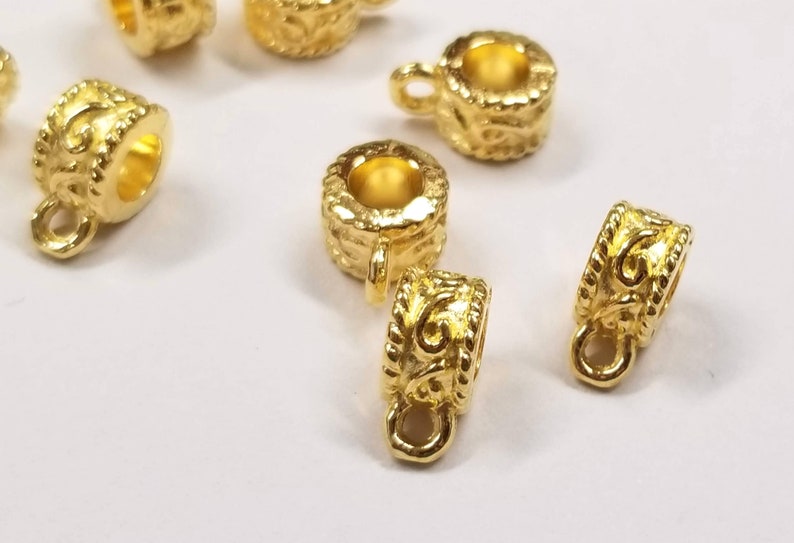 May include: Gold-toned metal pendant bails with a decorative design. The bails have a loop at the top for attaching a pendant and a small loop at the bottom for attaching a chain.