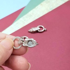 May include: Two silver magnetic clasps for jewelry making. The clasps are round and have a small, flat, silver magnet on one side.