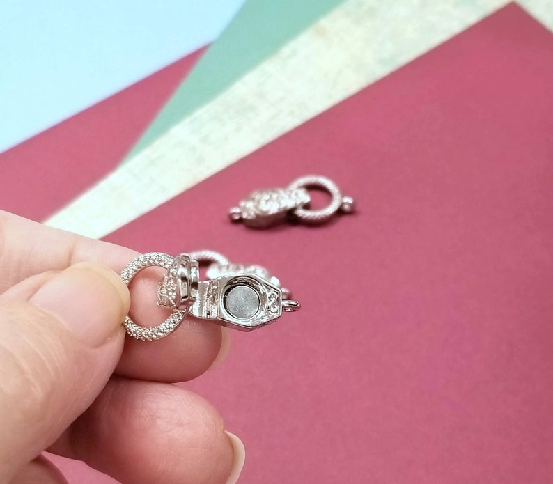 May include: Two silver magnetic clasps for jewelry making. The clasps are round and have a small, flat, silver magnet on one side.