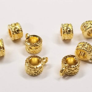May include: Eight gold-toned metal bead caps with an ornate design. The bead caps have a small loop on one side for attaching to jewelry.