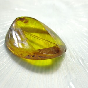 May include: A yellow, oval-shaped, glass bead with a clear center and a darker yellow outer edge.