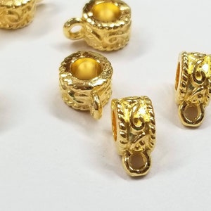 May include: Gold-toned metal bead caps with a decorative swirl design. The caps have a small loop on the bottom for attaching to jewelry.