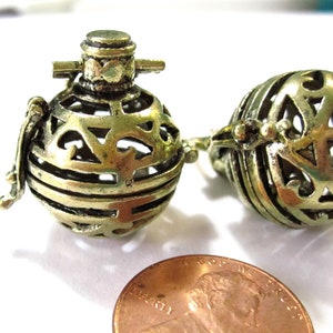 May include: Two gold-toned metal cage-like ornaments with intricate designs. The ornaments are about the size of a US penny.