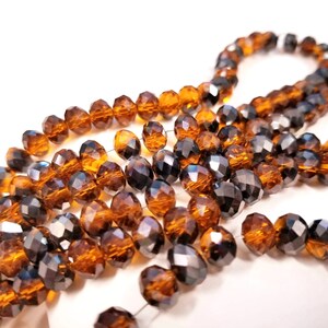 May include: A strand of faceted glass beads in a mix of amber and black colors. The beads are strung on a clear thread and have a shiny, iridescent finish.