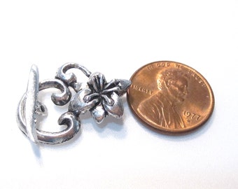 May include: Silver-toned metal toggle clasp with a floral design. The clasp is about the size of a US penny.