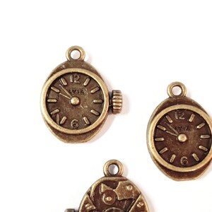 May include: Three antique gold-toned metal watch charms with clock faces. The charms have a vintage look and are perfect for adding a touch of whimsy to jewelry or crafts.
