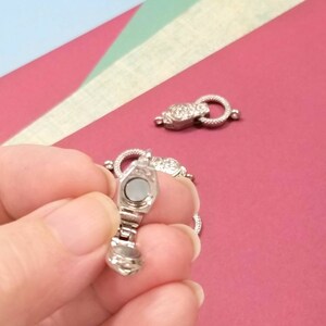 May include: Silver magnetic clasp for a necklace or bracelet. The clasp is open and shows the magnetic mechanism inside.