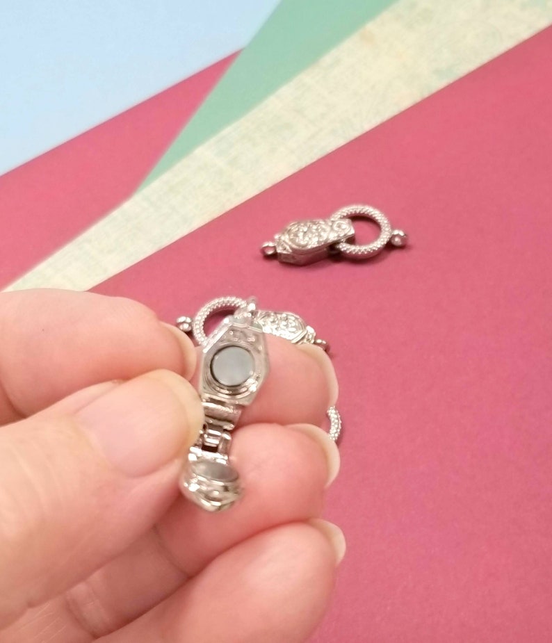 May include: Silver magnetic clasp for a necklace or bracelet. The clasp is open and shows the magnetic mechanism inside.