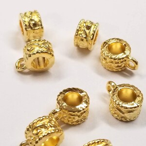 May include: Gold-toned metal bead caps with a decorative design. The bead caps have a small loop on one side for attaching to a necklace or bracelet.