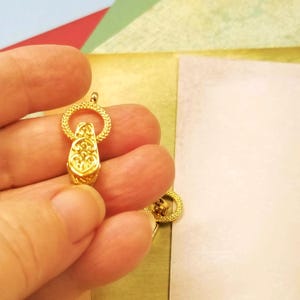 May include: Gold-toned metal clasp with a detailed floral design. The clasp is circular with a textured surface.