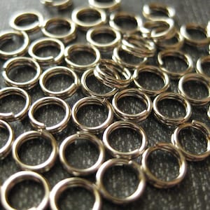 May include: A large pile of silver jump rings, a type of metal ring used in jewelry making.