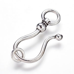 May include: Silver-toned metal hook clasp with a round loop at the top and a curved hook at the bottom. The hook has a small ball at the end.