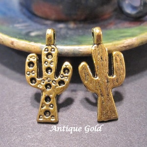 May include: Two antique gold cactus charms. The cactus on the left has a textured surface with small circles. The cactus on the right has a textured surface with vertical lines.  Antique Gold.