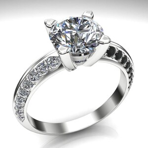 May include: A silver engagement ring featuring a large, round, clear diamond centre stone. The band is accented with smaller diamonds and black stones.