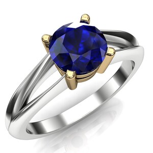 Op de afbeelding: Een zilveren en gouden ring met een blauwe saffier edelsteen. De ring heeft een gedraaide band.