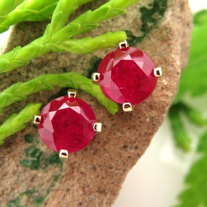 Pode incluir: Um par de brincos de rubi com engastes de ouro. Os rubis são redondos e têm uma cor vermelha intensa.