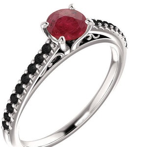 May include: A silver ring featuring a large, round, red gemstone as the centerpiece. The band is adorned with small, black gemstones and decorative filigree. A classic and elegant piece of jewelry.