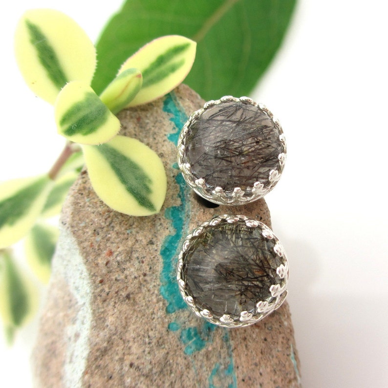 May include: A pair of silver earrings featuring round, clear, black, and silver stones. The stones are set in a silver bezel with a scalloped edge.