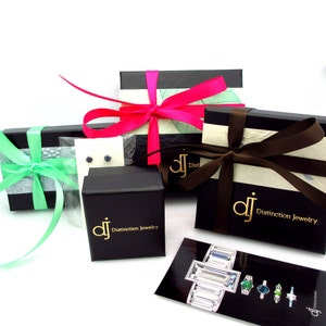 May include: Four black gift boxes with different coloured ribbons. The boxes are tied with green, pink, brown, and white ribbons. The boxes have the text "Distinction Jewelry" printed on them.
