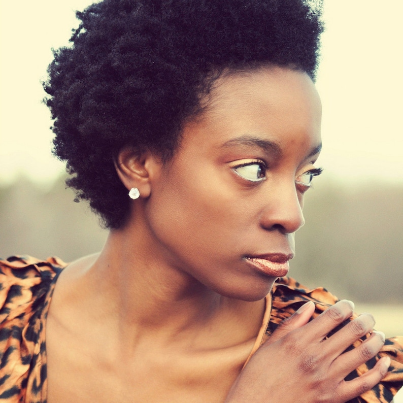 May include: A woman with short, curly black hair wearing a brown and black animal print top. She is looking off to the side with a thoughtful expression.
