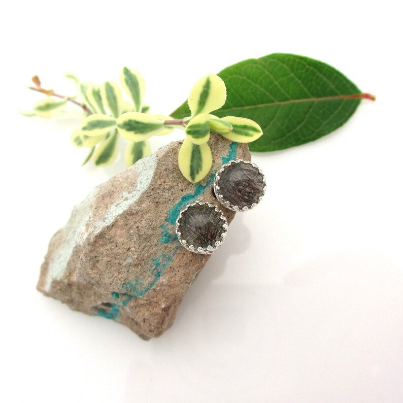 May include: A pair of silver stud earrings with a round, dark grey stone set in a silver bezel. The stones have a sparkly, iridescent quality.
