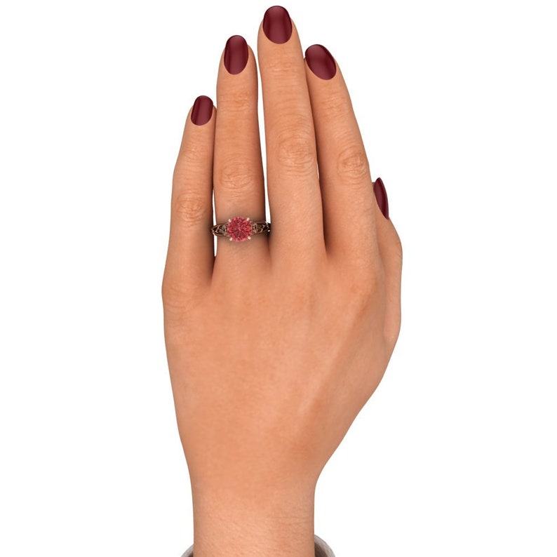 Puede incluir: Un anillo de compromiso de oro rosa con una piedra preciosa rosa rodeada de piedras m&aacute;s peque&ntilde;as. El anillo est&aacute; en el dedo de una modelo.