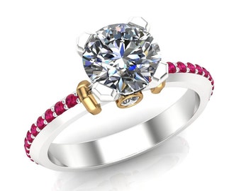 May include: A silver and gold engagement ring with a large, round, clear diamond center stone. The band is accented with a row of small, red gemstones.