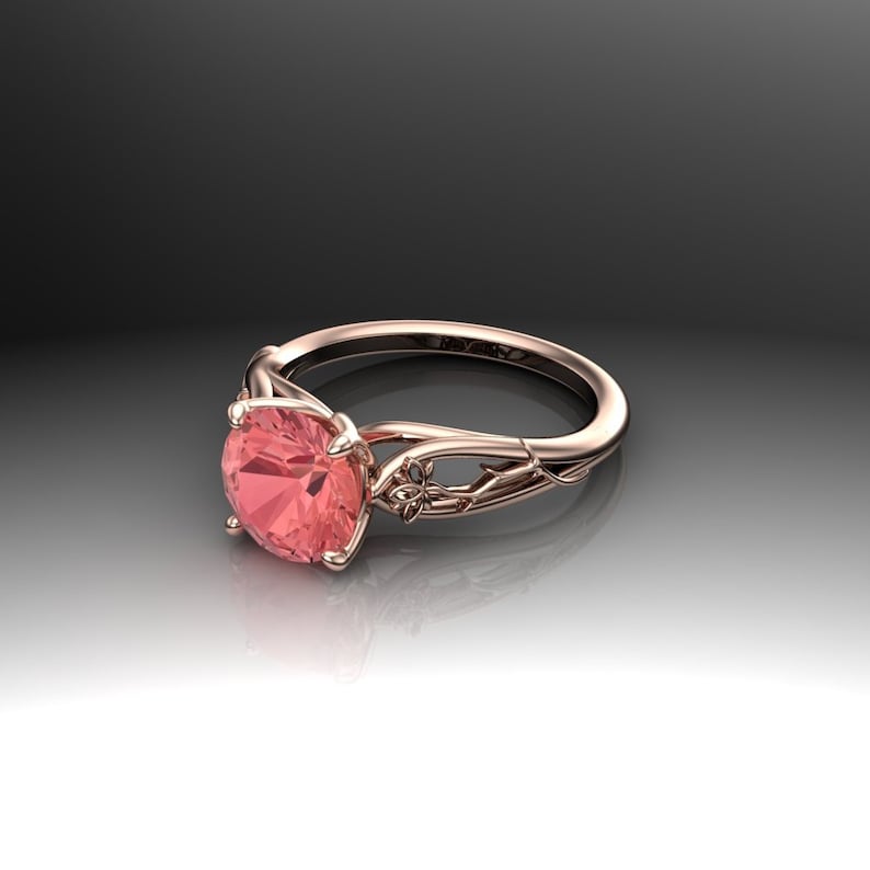 Puede incluir: Un anillo de compromiso de oro rosa con un delicado dise&ntilde;o floral y una piedra preciosa rosa redonda.