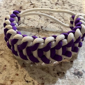 May include: A braided dog collar in a pattern of white and purple. The collar is made of thick, woven rope and has a simple design. The collar is designed to be worn around a dog's neck.