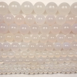 May include: Close-up of several strands of pale pink and white gemstone beads. The beads are spherical and vary in size, from large at the top to small at the bottom. The beads have a polished finish and a translucent quality.