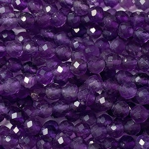 May include: Close-up of faceted, deep purple amethyst beads. The beads are round with multiple facets that catch the light, creating a sparkling effect. The beads are strung together, suggesting they are for jewelry making or crafting.