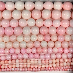 Puede incluir: Filas de cuentas redondas y pulidas en varios tonos de rosa y blanco llenan el marco. Las cuentas varían en tamaño, creando un efecto degradado. Las cuentas son probablemente para la fabricación de joyas.