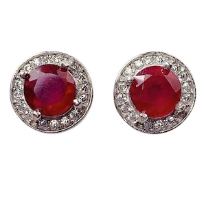 May include: A pair of silver stud earrings with a red gemstone surrounded by a halo of smaller white gemstones.