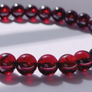 Puede incluir: Un brazalete de piedras preciosas rojas con cuentas redondas. El brazalete est&aacute; hecho de piedras naturales y tiene un acabado pulido.