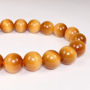 May include: A bracelet made of round, golden brown beads. The beads have a subtle shimmer.
