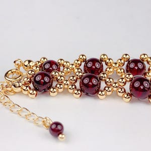 May include: A gold bracelet with red gemstone beads. The bracelet has a lobster clasp and a small chain extension.