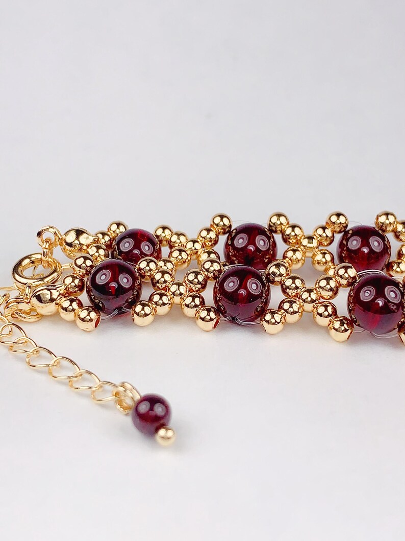 May include: A gold bracelet with red gemstone beads. The bracelet has a lobster clasp and a small chain extension.