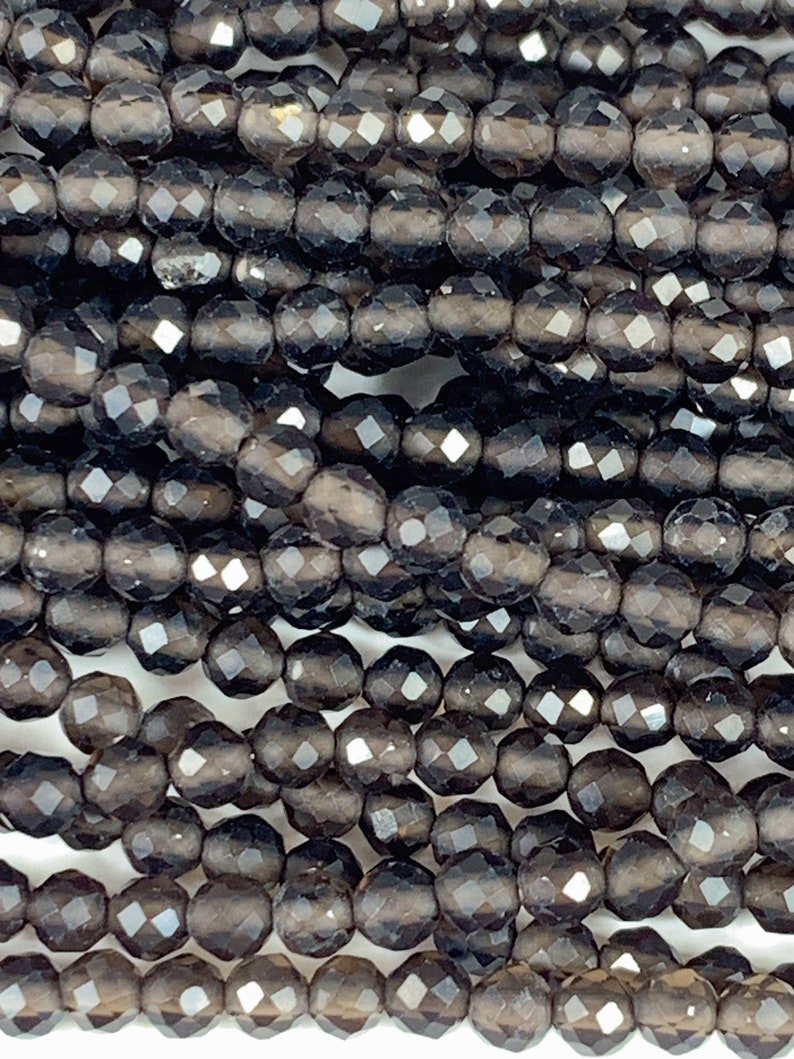 May include: A strand of dark gray faceted gemstone beads. The beads are round and have a smooth, polished finish.