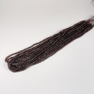 May include: A strand of dark brown faceted gemstone beads. The beads are strung on a thin thread and are ready to be used for jewelry making.